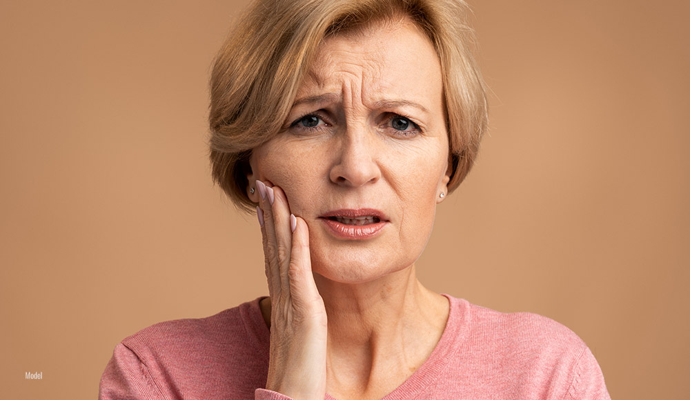 close-up of woman holding her face, clenching her teeth in pain.